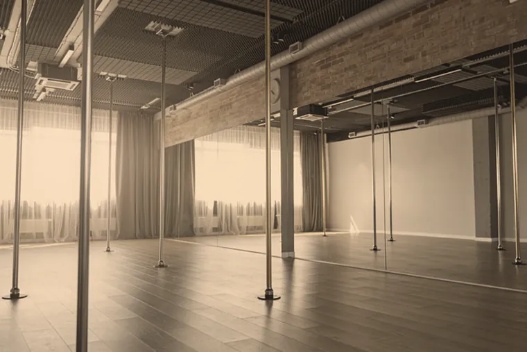 Salão amplo com várias barras de pole dance, tijolo aparente e luz natural